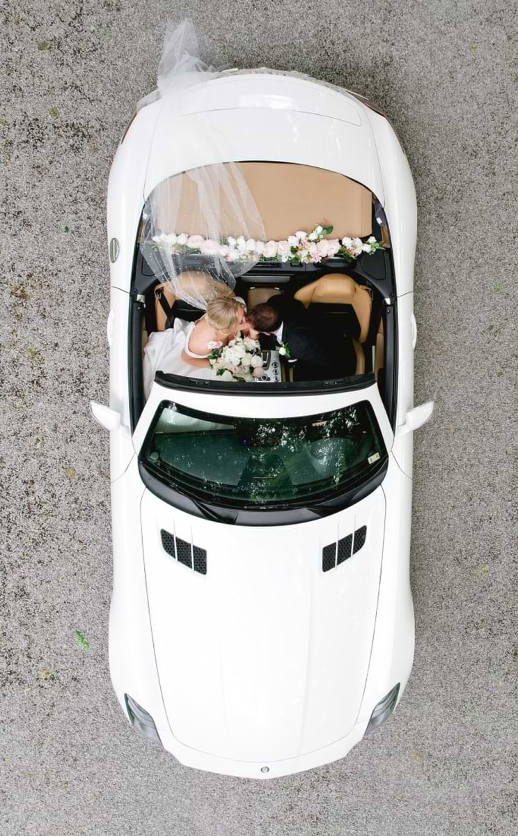 overhead shot looking down at the bride and groom in a white convertible car