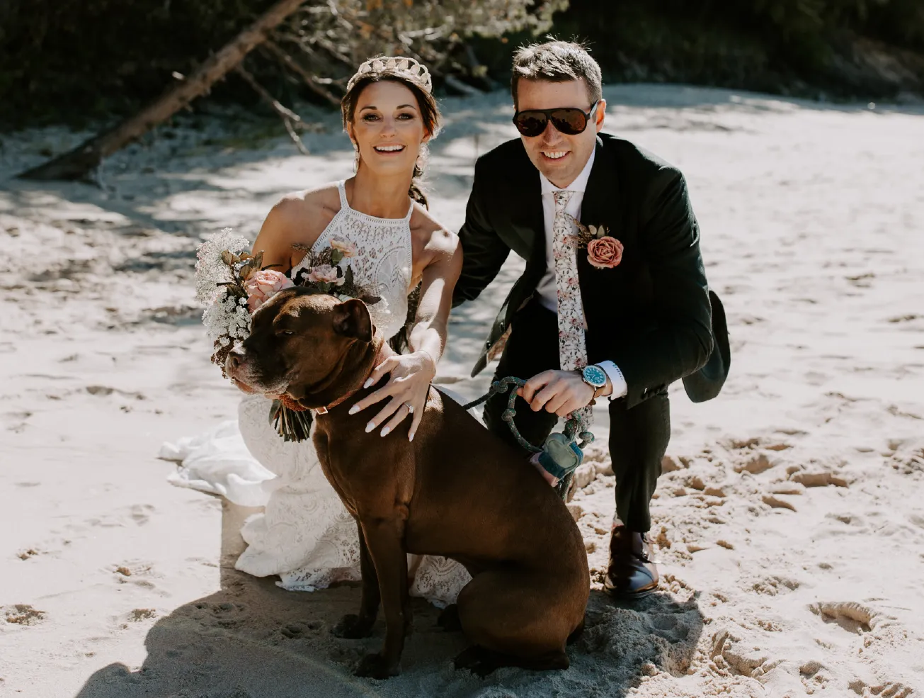 Rachel and Andrew kneeling with their dog on sand