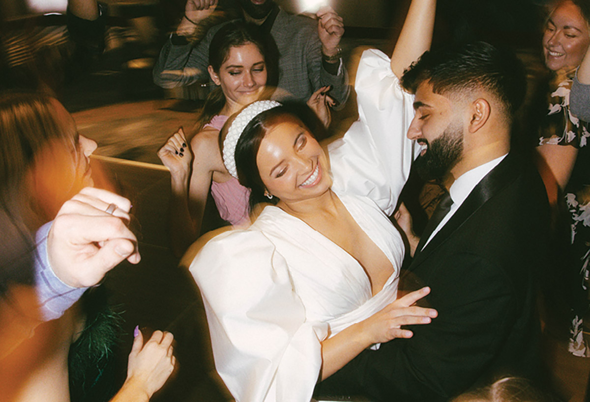 Close-up photograph perspective of a group of people dancing full of joy close by each other with the bride and groom dancing in the middle smiling inside the JW Marriott Grand Rapids venue