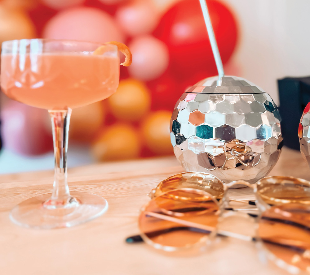 close up of a full cocktail glass, a disco ball cup with a straw, and sets of sunglasses