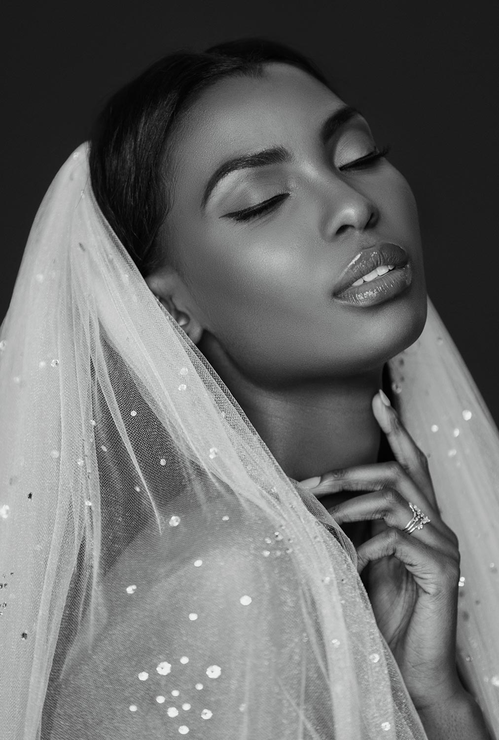 black and white image; a woman with her head slightly tilted back and her eyes closed wears an Ariel Taub Nova fingertip bubble veil embellished with Austrian crystals and a diamond ring