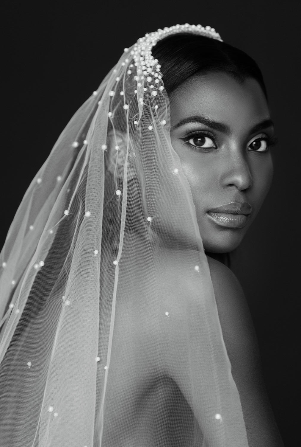 black and white portrait of a woman looking over her shoulder at the camera while wearing a CHOSEN by Kyha Marseille pearl veil