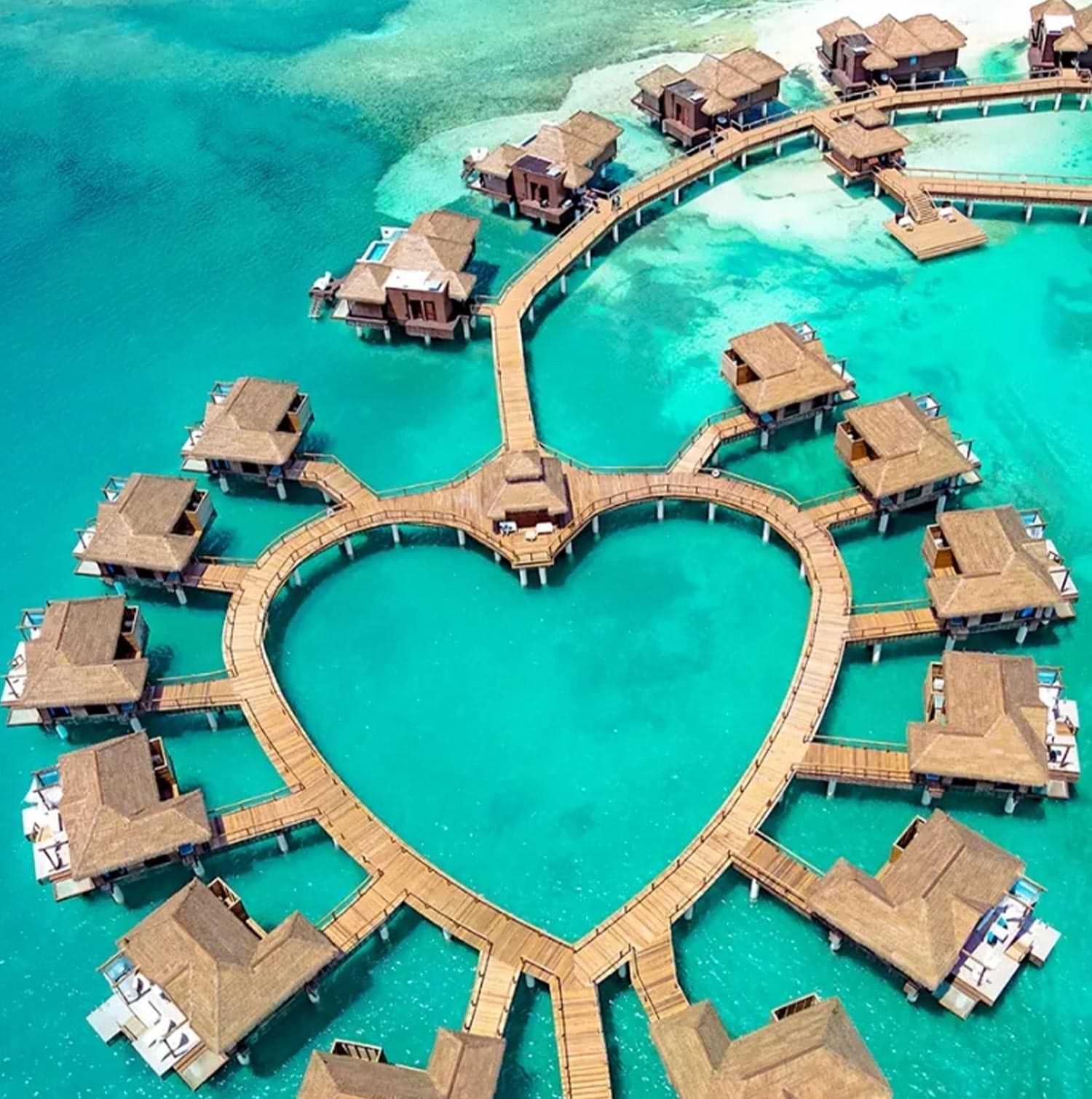 aerial view of bungalows over white sand beach water, the pathway to each bungalow creates the shape of a heart