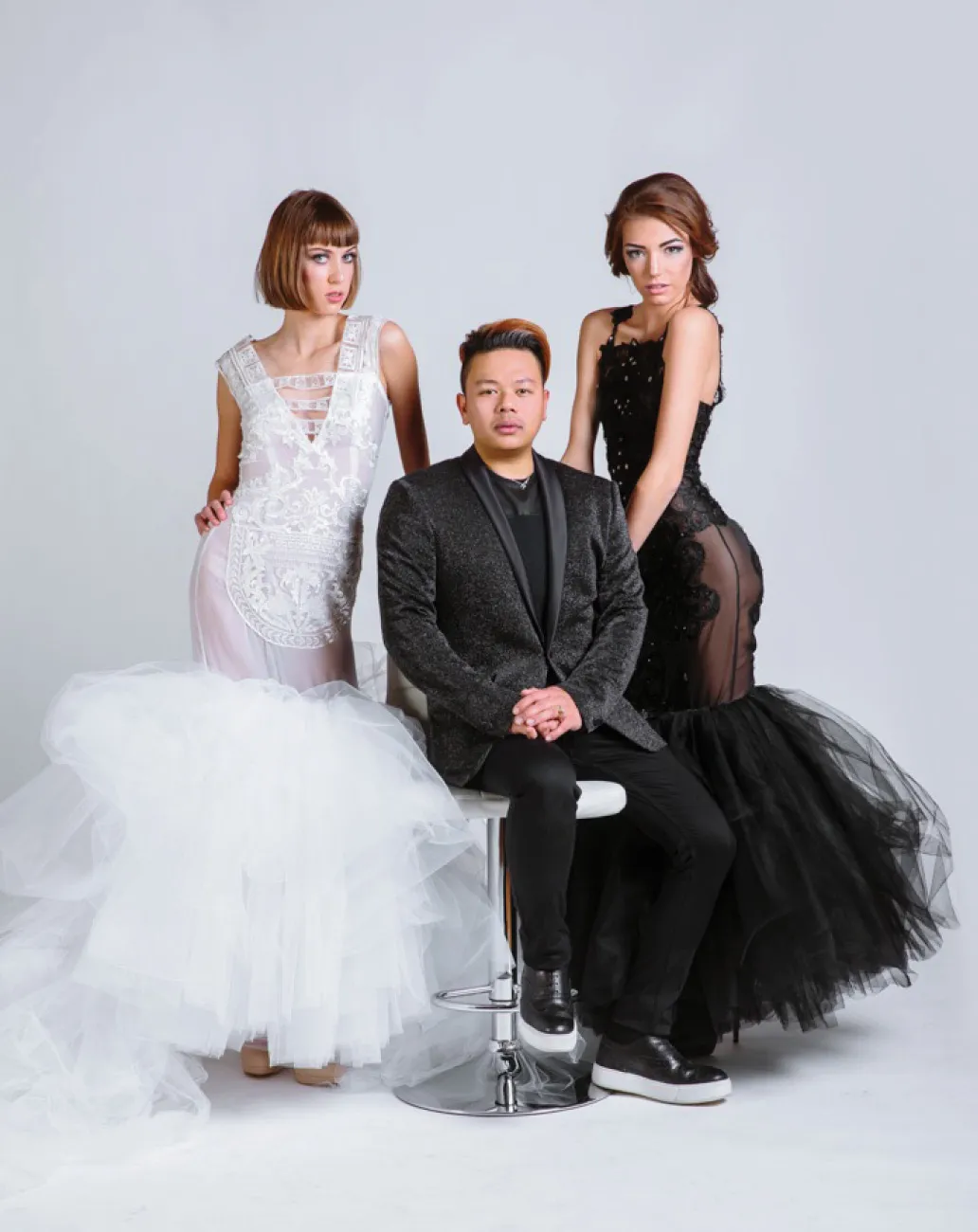 From left woman with lacey white dress, man sitting in black suit and woman in lace black dress
