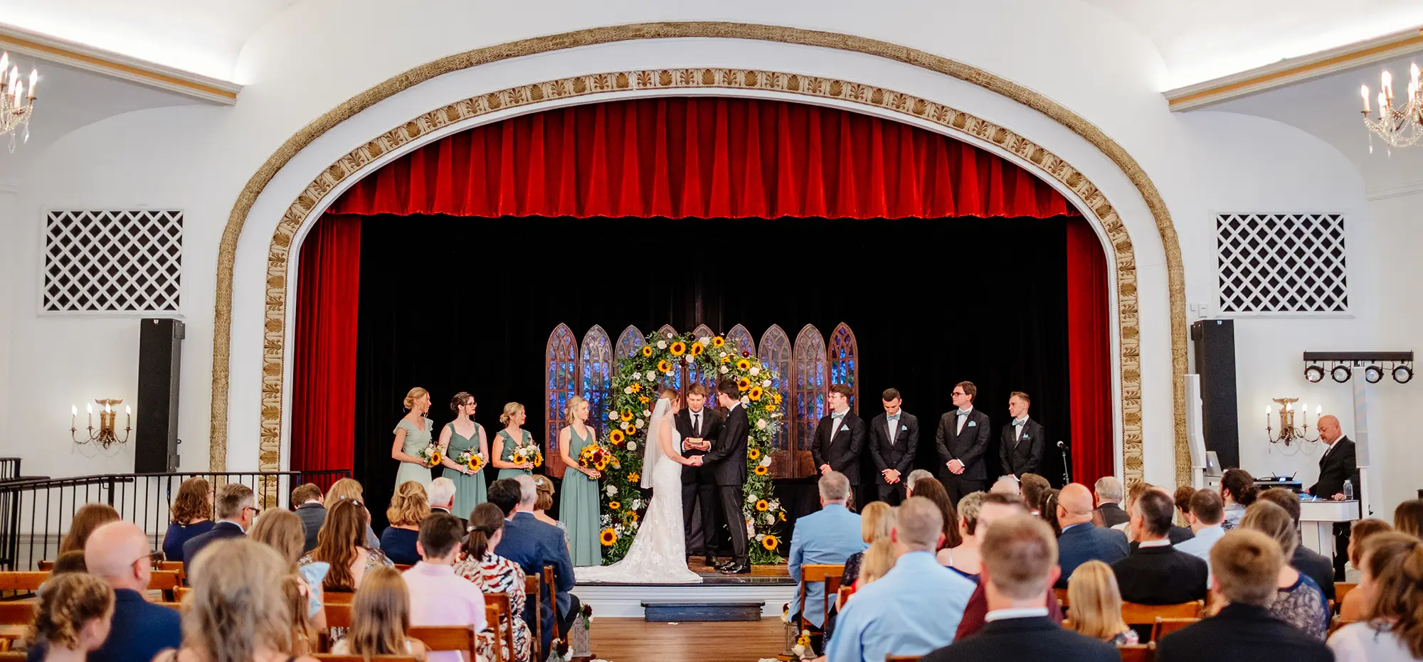 Wedding ceremony in session with the bride and groom on a stage as the audience glances upon them inside The Ladies' Literary Club building