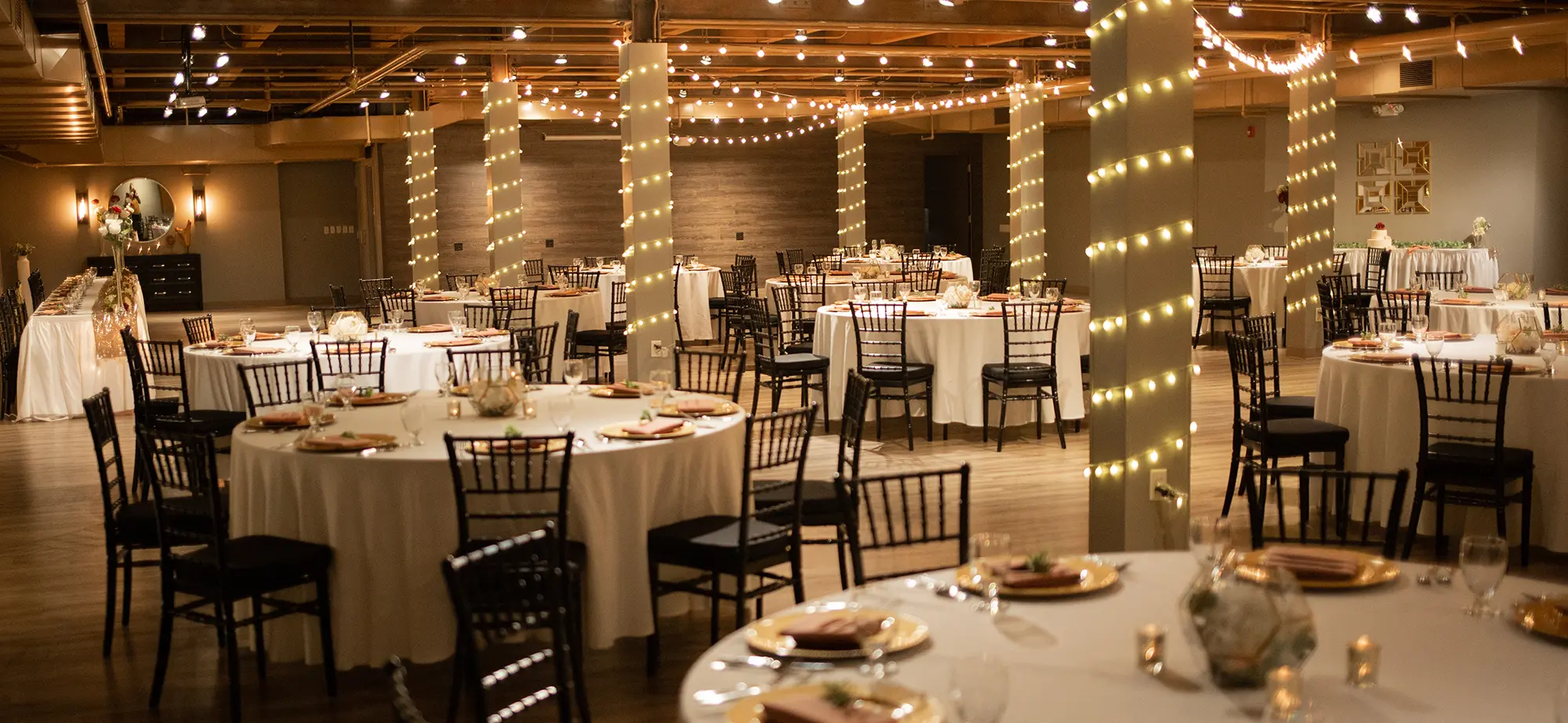Large room area with white tables and black chairs inside The Waddell Center venue with numerous light decorations all around