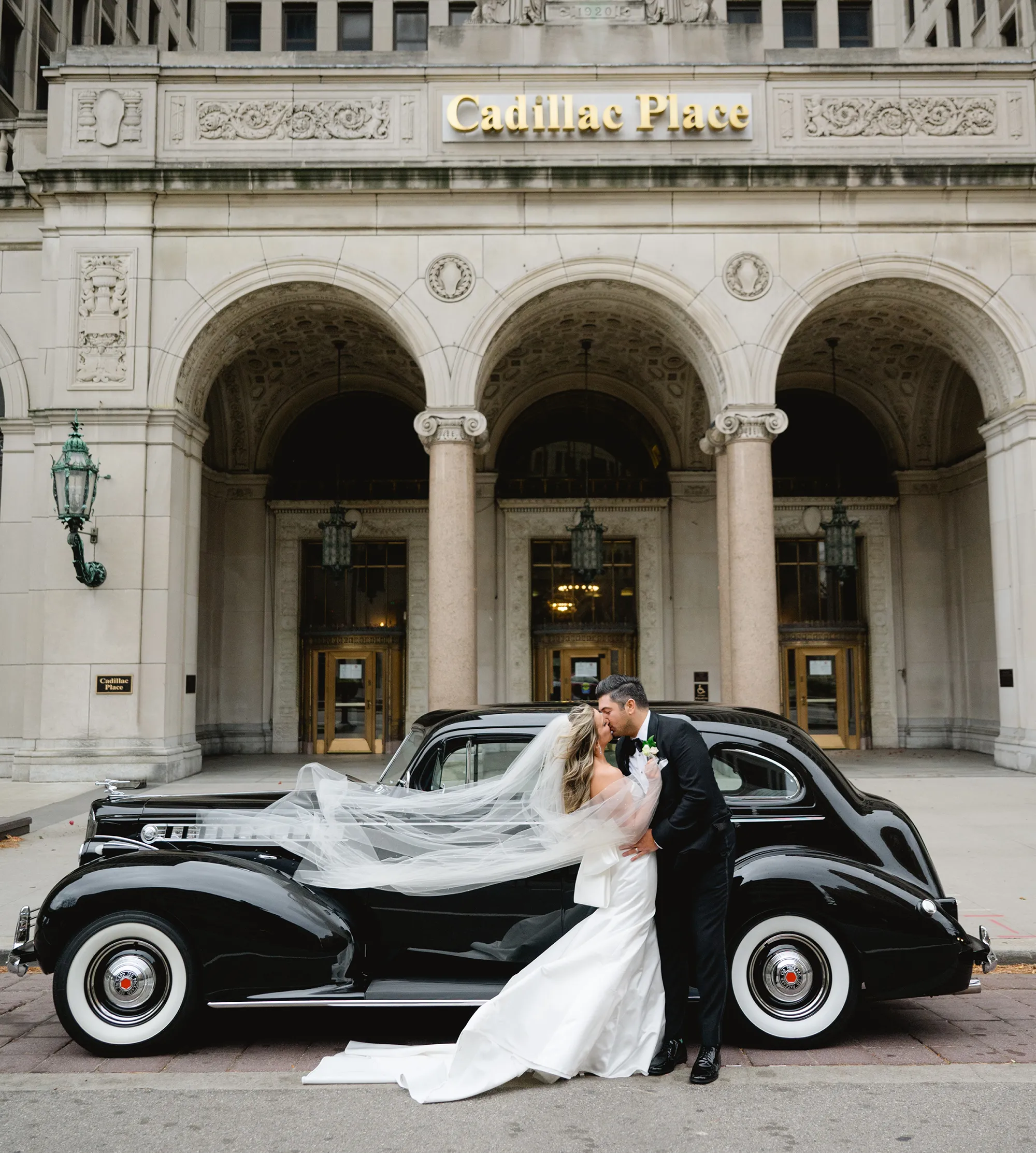 Jaclyn and Nick kissing in front of old car and Cadillac building
