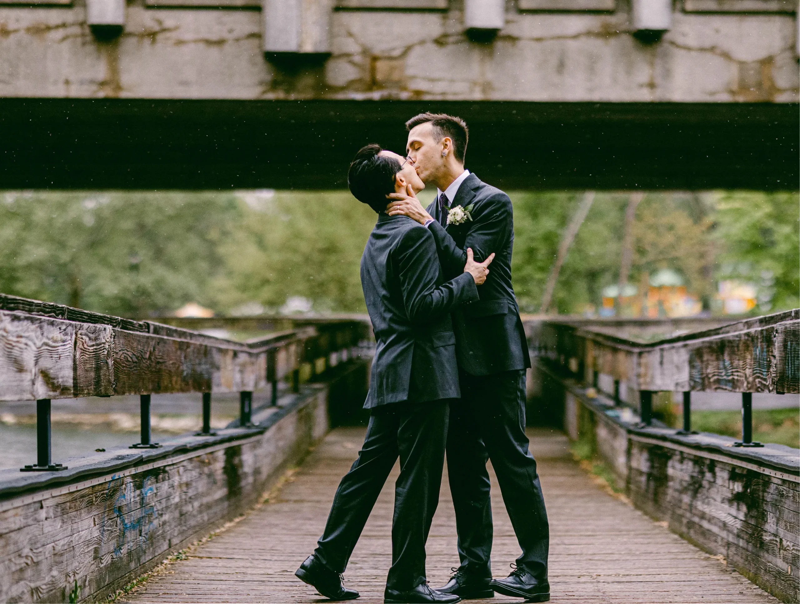 grooms kissing in front of a bridge