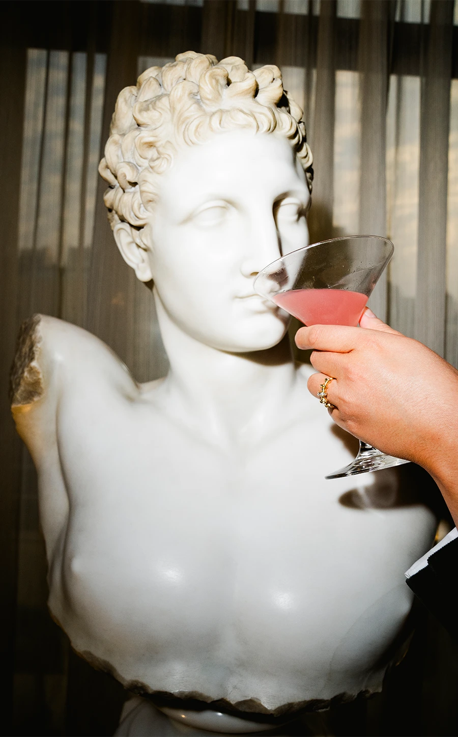 hand holding up a martini glass to a statue decoration
