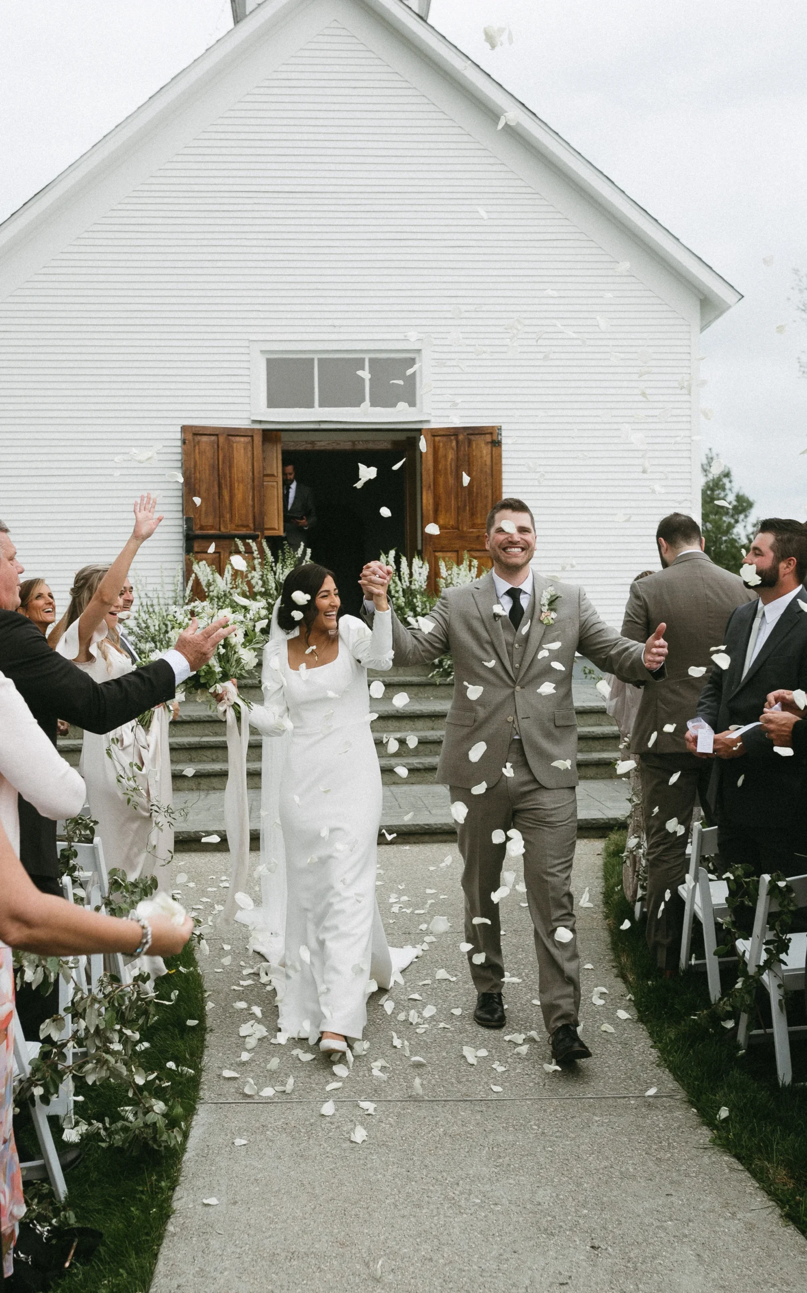 bride and groom walking out of venue while guests throw flower petals in the air