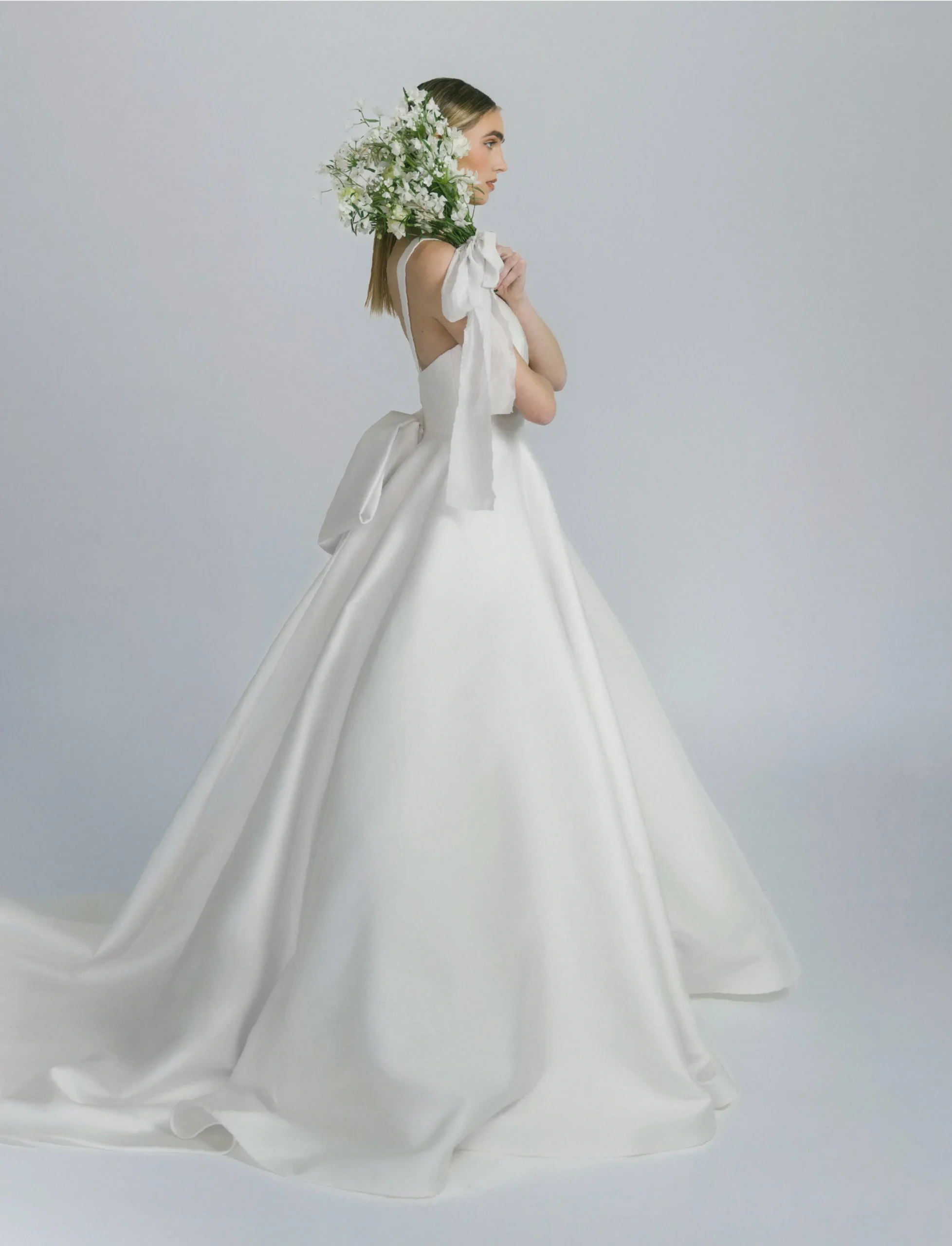 Bride holding bouquet, back of open wedding dress.