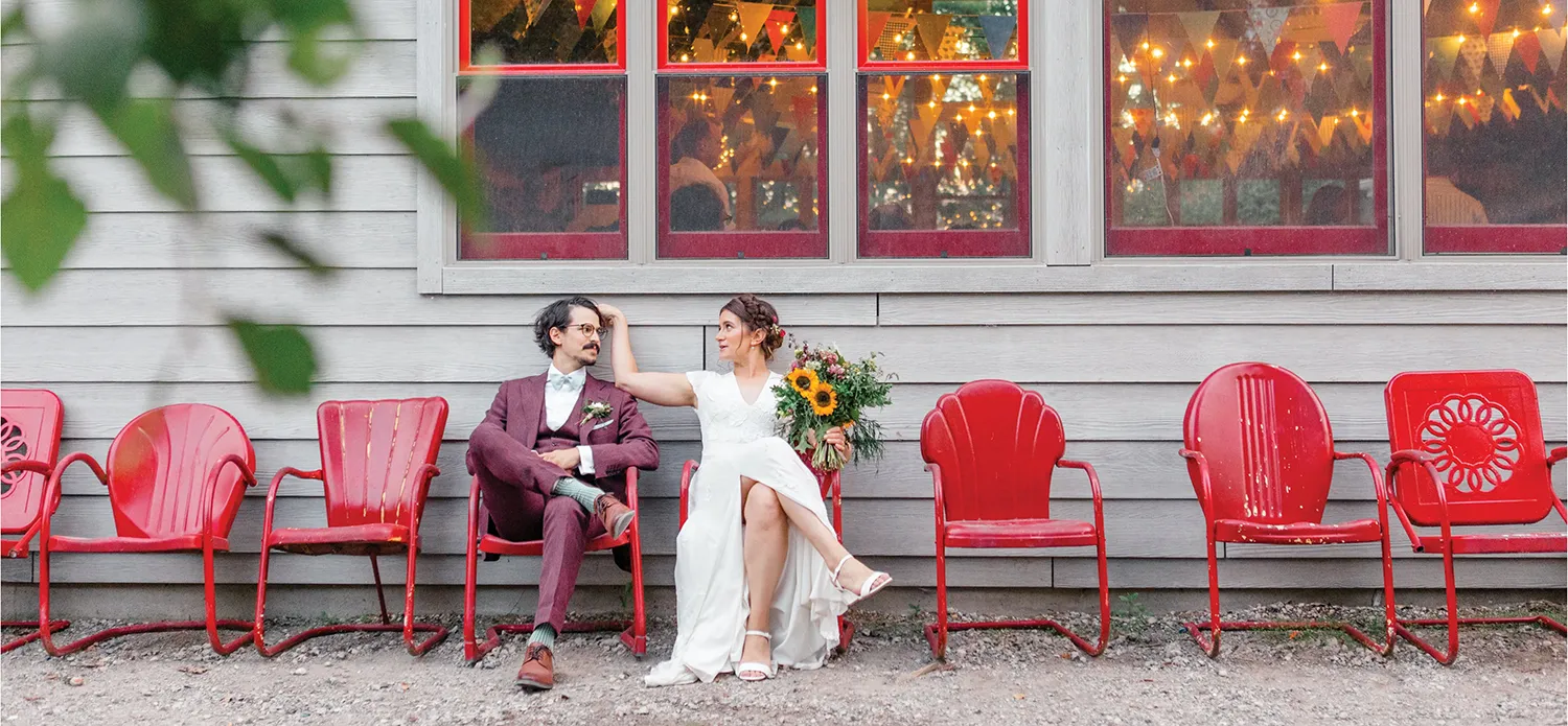 bride and groom outside of venue in red chairs