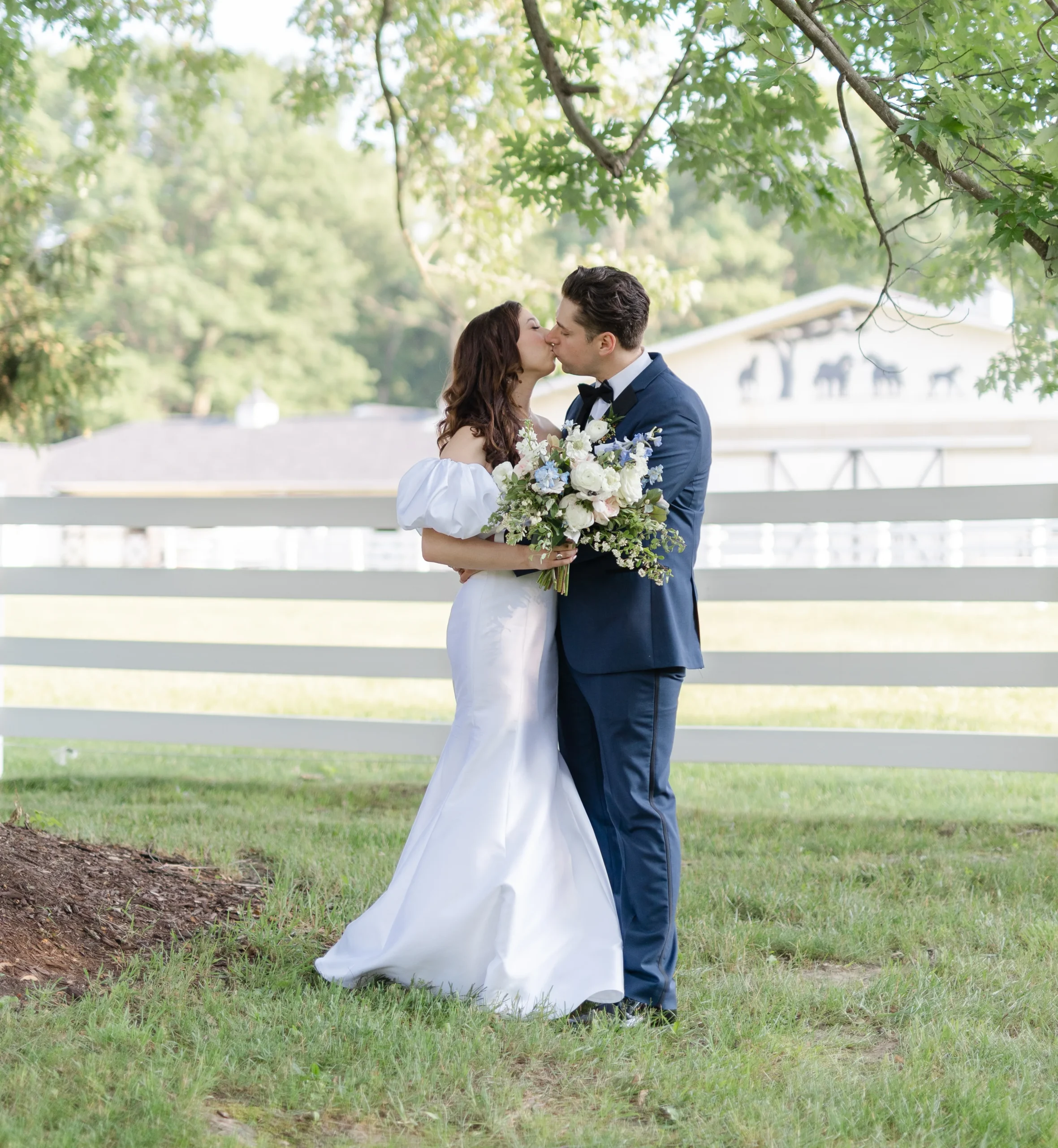 bride and groom kissing under tree in front of white fence