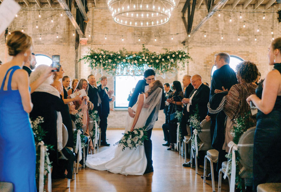 couple kiss in the middle of the aisle surrounded by their clapping guests