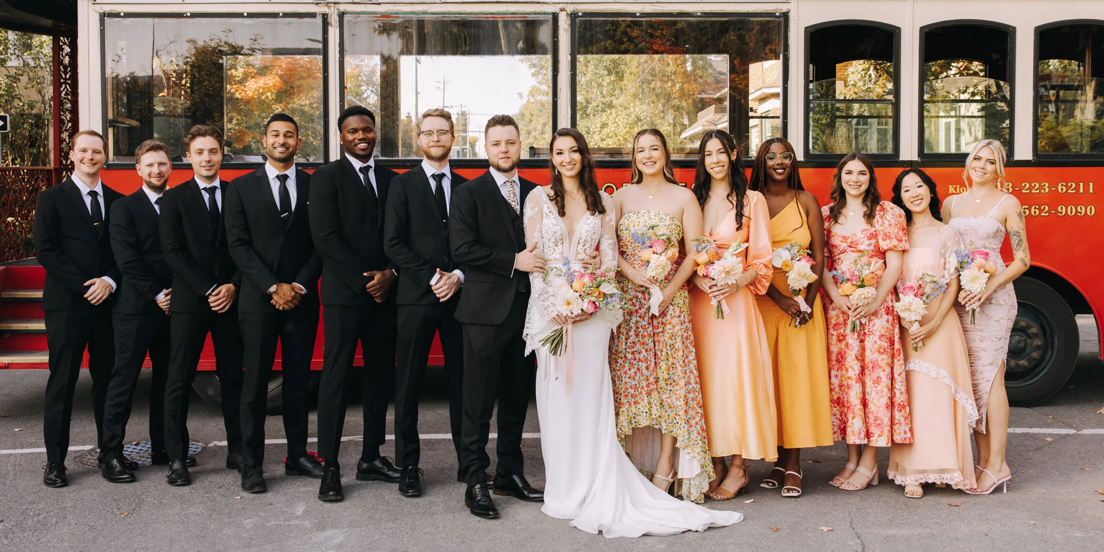 bride and groom surrounded by their groomsmen and bridesmaids standing in front of a bus