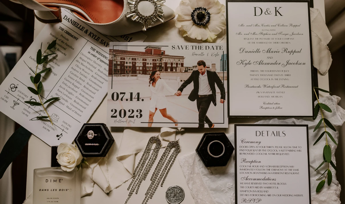 wedding invitation, save the date, rings, and itinerary displayed on table with flowers, perfume, heels, and jewelry