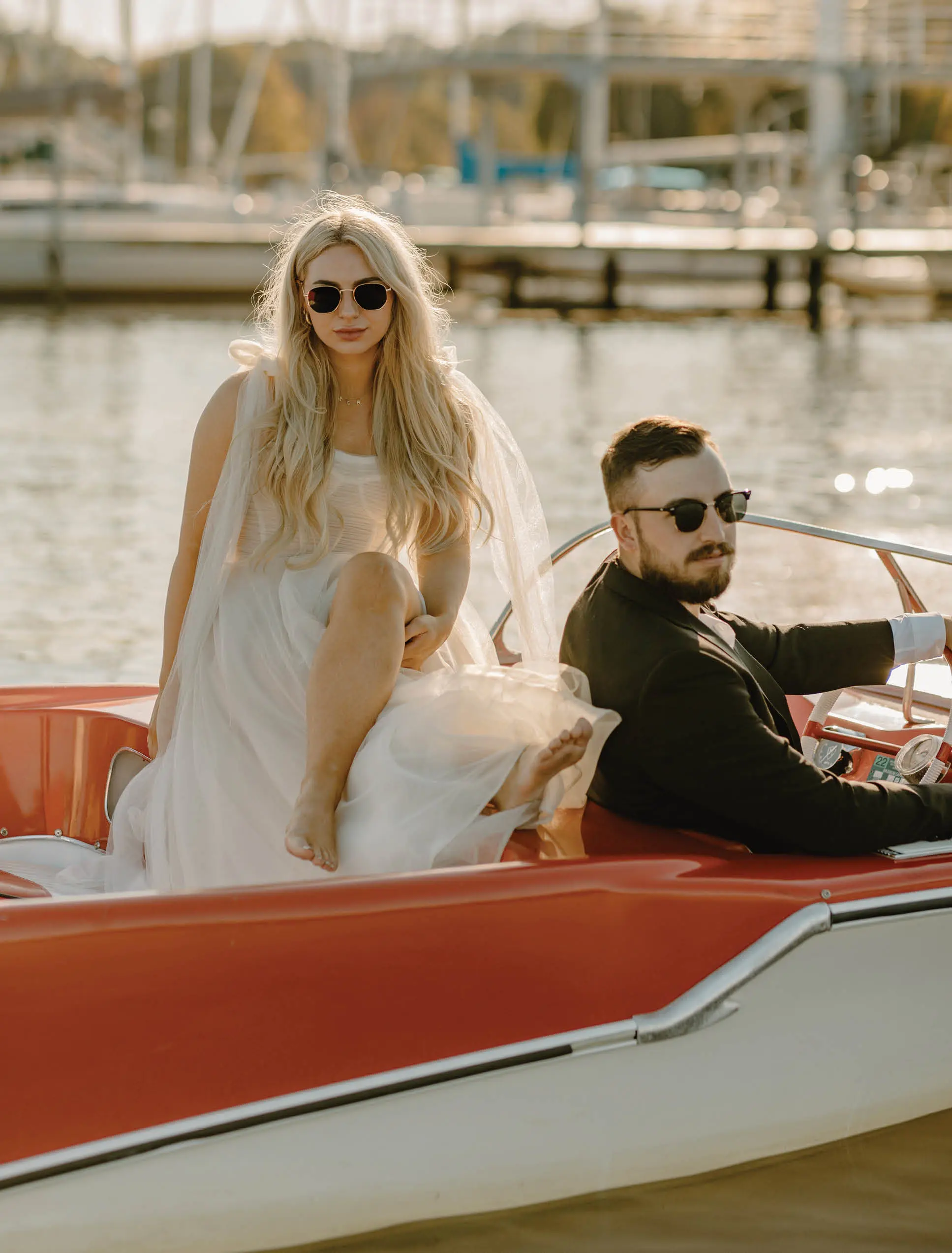 man and woman with sunglasses and straight faces sitting in a red speed boat