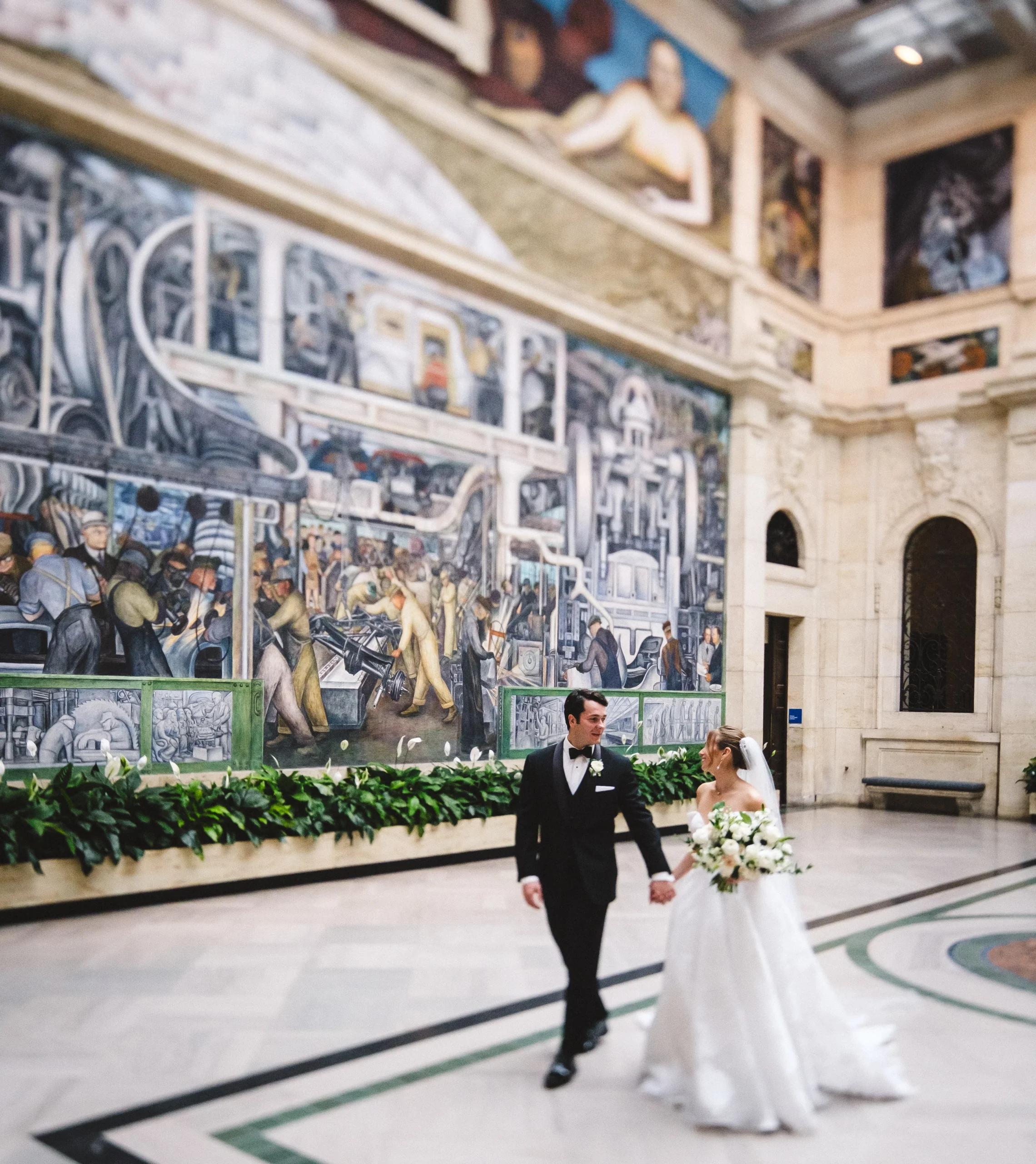 bride and groom holding hands while walking through a building with multiple murals on the walls