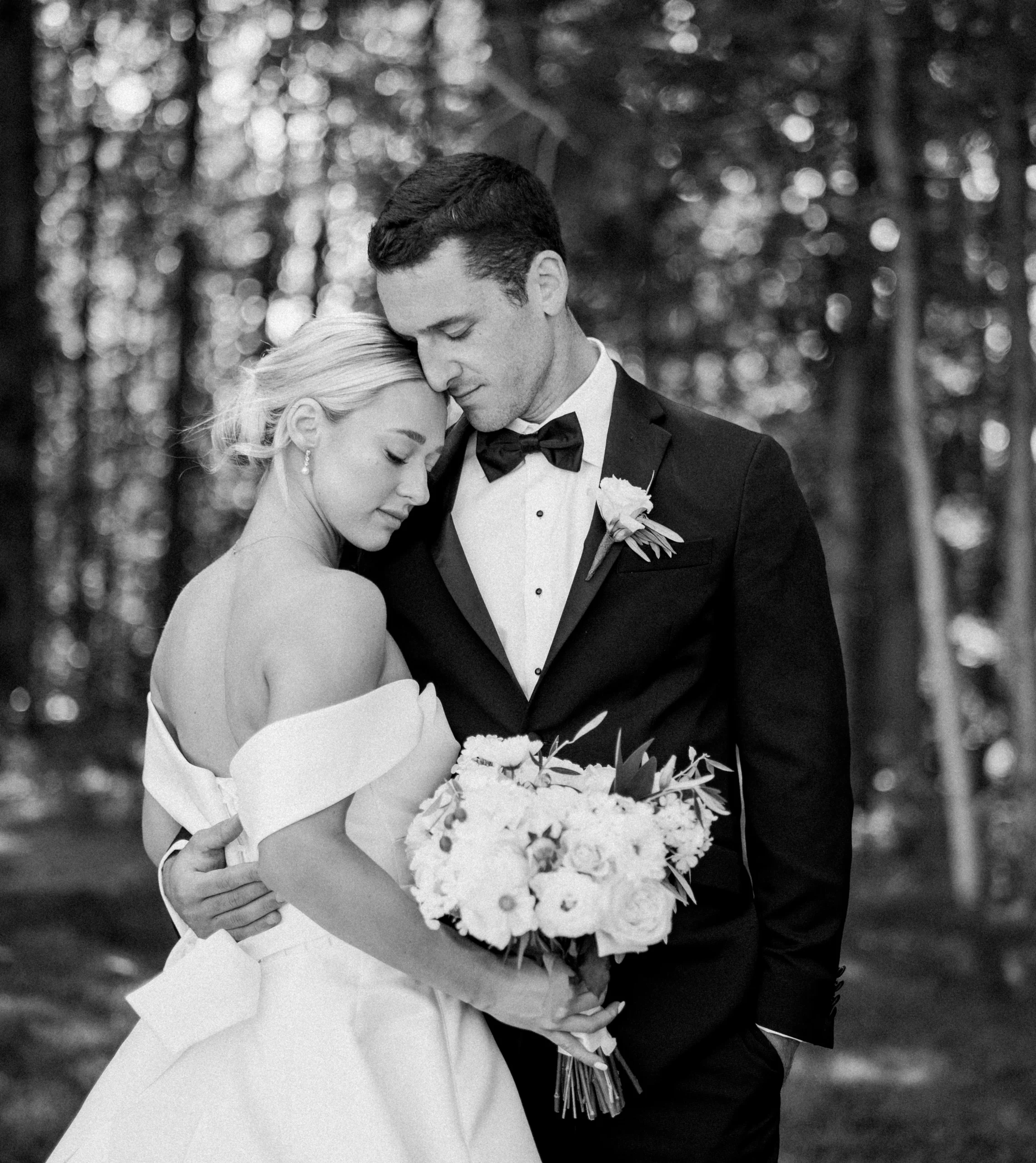 black and white picture of bride and groom hugging in wooded area 