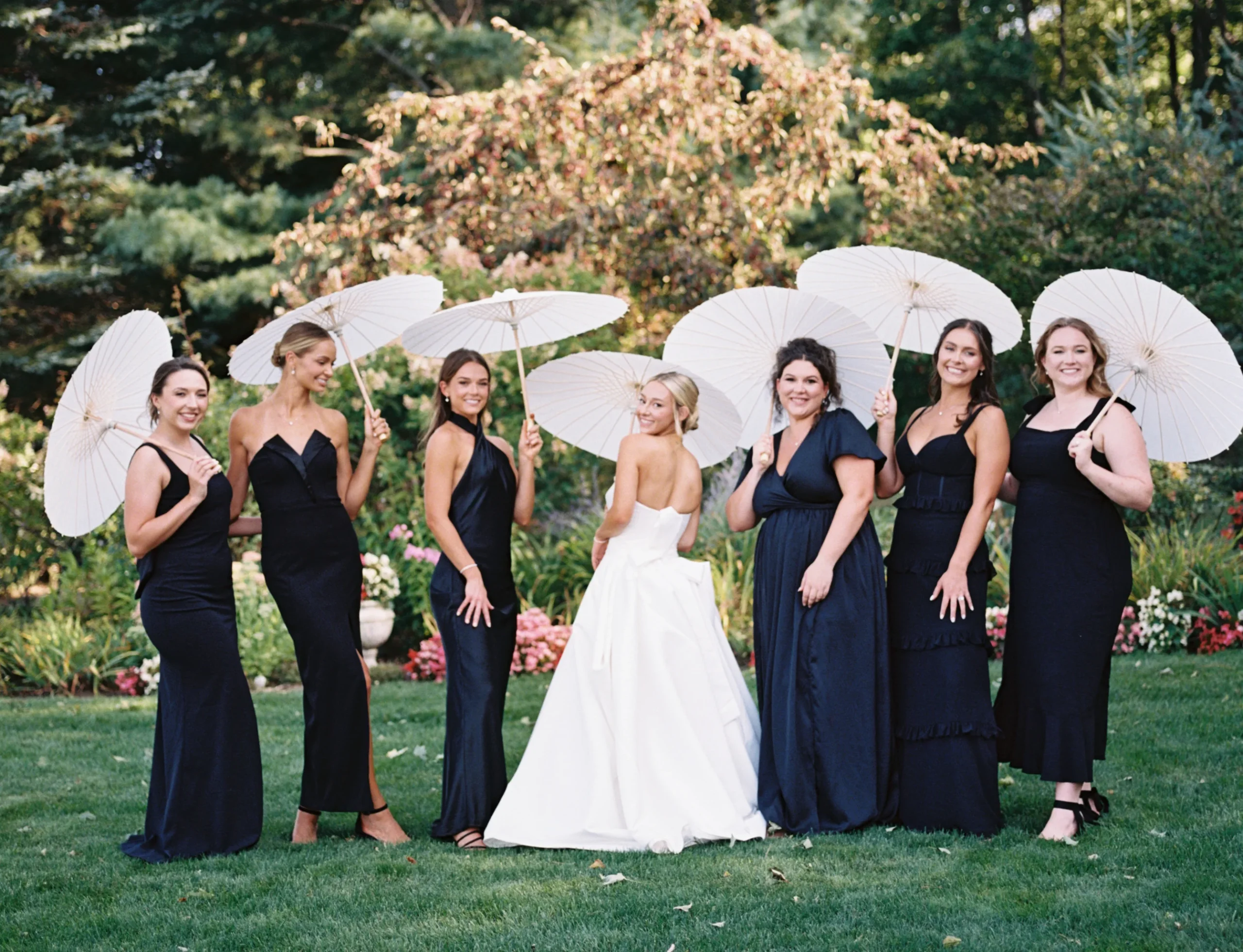 bride posing with her bridesmaid while holding white parasols 